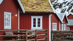 Rotes skandinavisches Holzhaus mit weißen Fensterrahmen und einem Grasdach